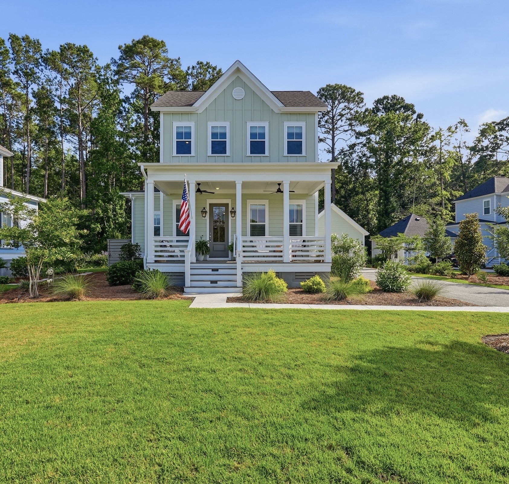 Green two-story Lowcountry home with white front porch and American flag on a manicured lawn